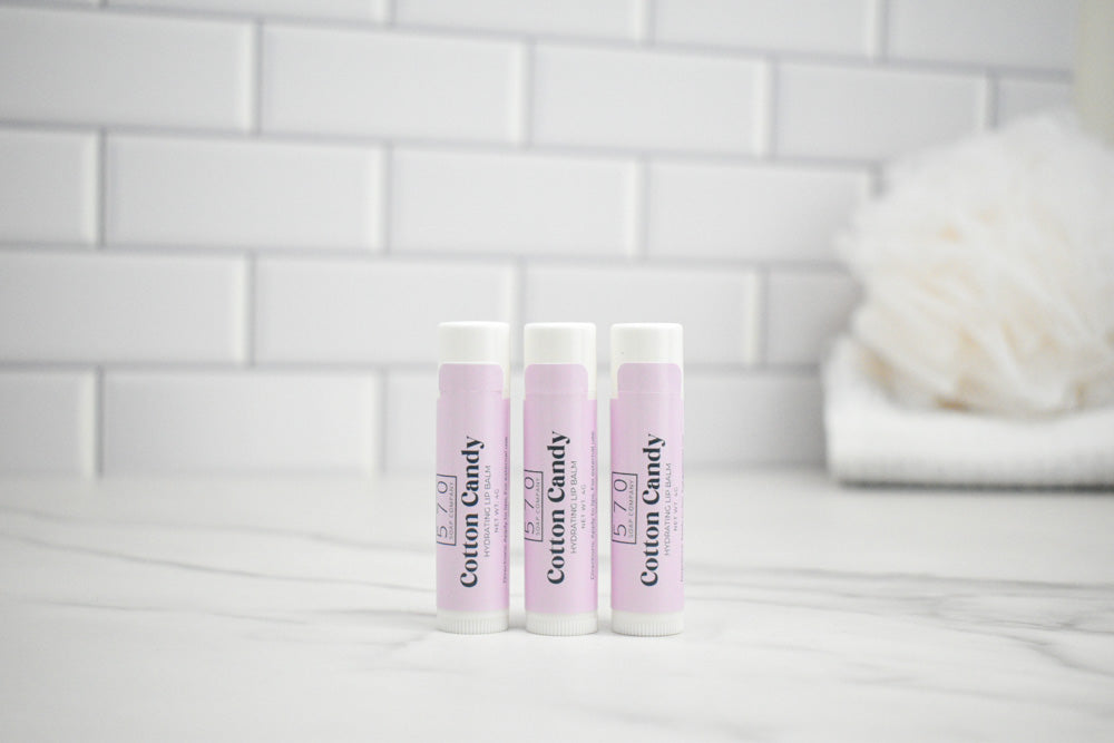 Three lip balm tubes with 'Custom Candy' branding on a bathroom counter.