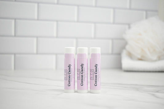 Three lip balm tubes with 'Custom Candy' branding on a bathroom counter.