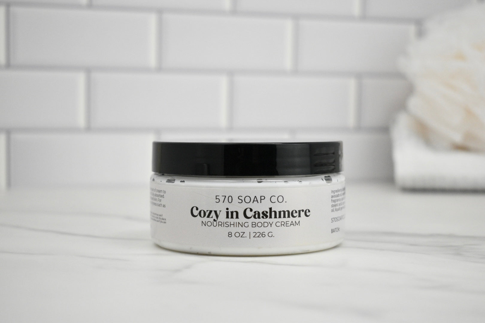 Jar of Cozy in Cashmere body cream by 570 Soap Co. on a bathroom counter.