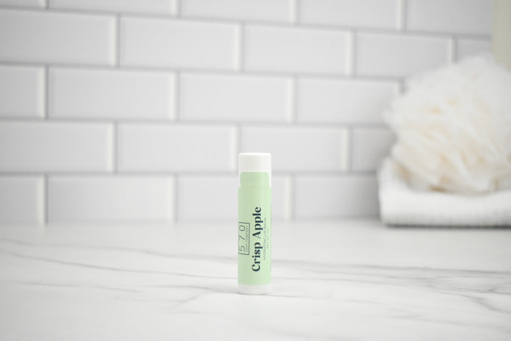 Lip balm with 'Crisp Apple' flavor on a white surface with a tiled wall background