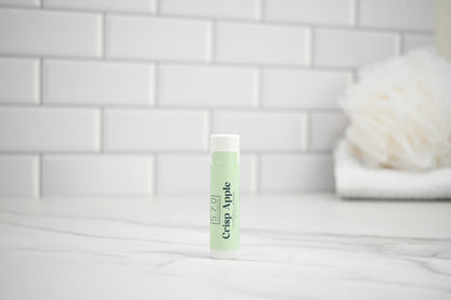 Lip balm with 'Crisp Apple' flavor on a white surface with a tiled wall background