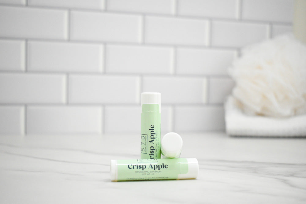 Two lip balms labeled 'Crisp Apple' on a bathroom counter with a tiled wall background.