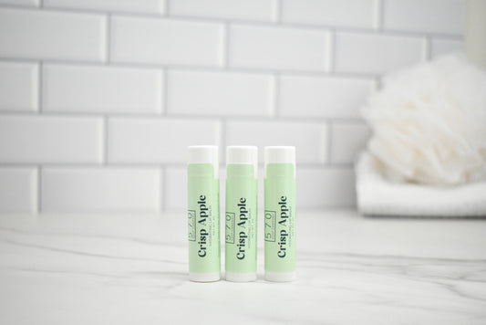 Three lip balm tubes labeled 'Crisp Apple' on a white surface with a tiled wall background.