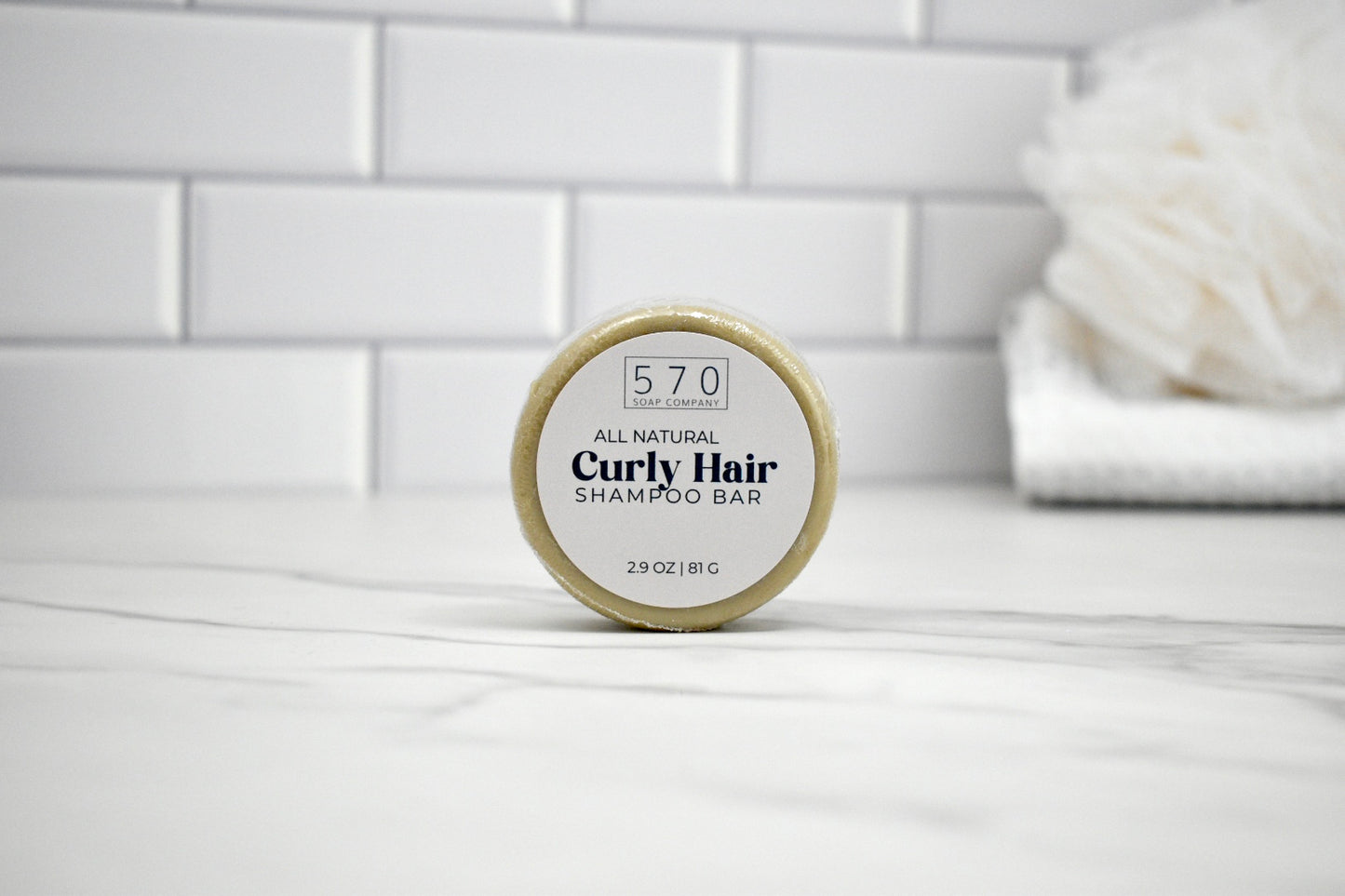 All natural curly hair shampoo bar on a white surface with a tiled wall background