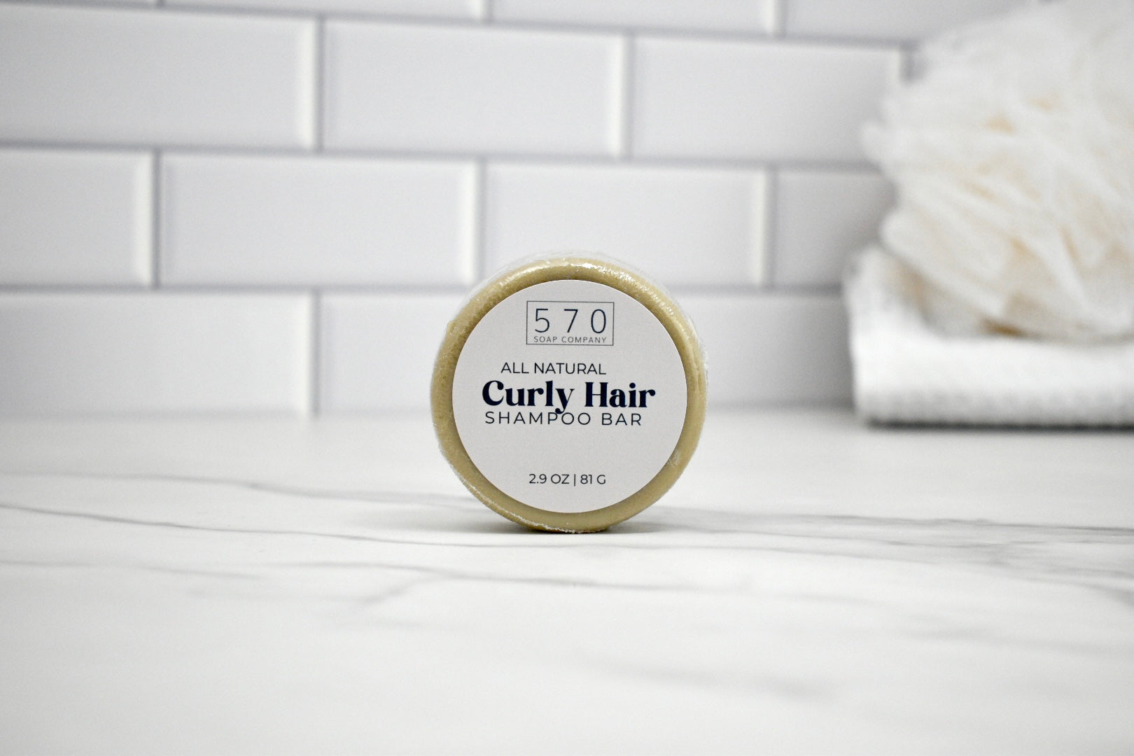 All natural curly hair shampoo bar on a white surface with a tiled wall background