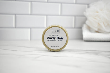 All natural curly hair shampoo bar on a white surface with a tiled wall background