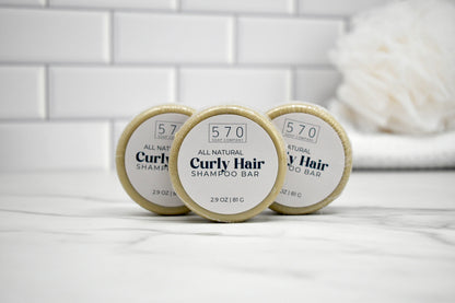 Three '570' curly hair shampoo bars on a white surface with a tiled wall background.