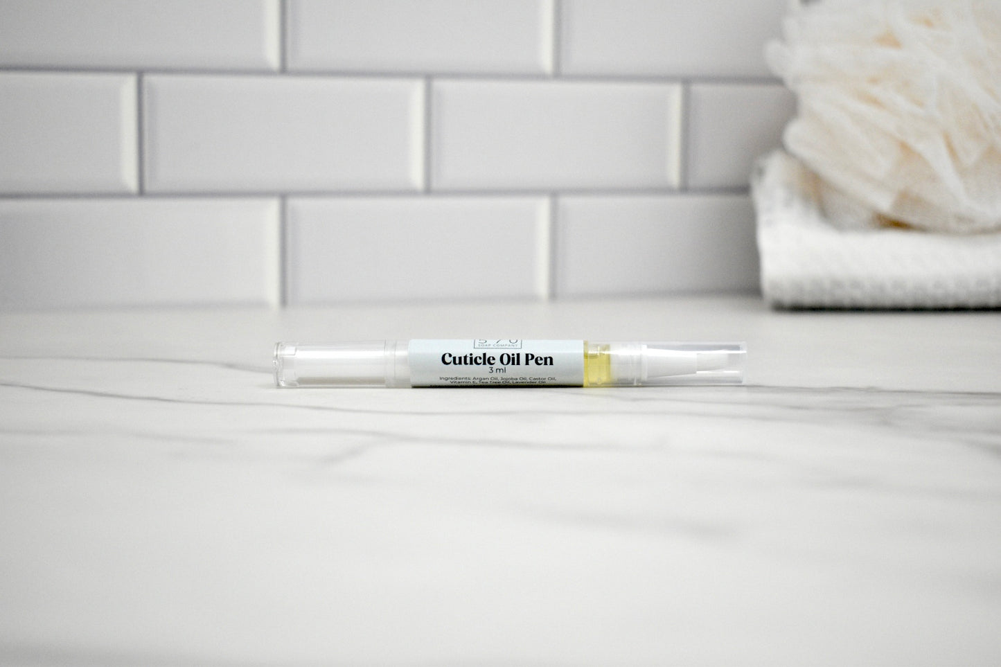 Cuticle oil pen on a bathroom counter with tiled wall in the background
