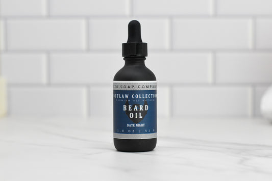 A 1.8 oz (51 g) bottle of 570 Soap Co.'s Beard Oil, labeled Date Night and featuring natural oils for premium beard care, comes with a dropper cap and sits elegantly on a white tiled surface.