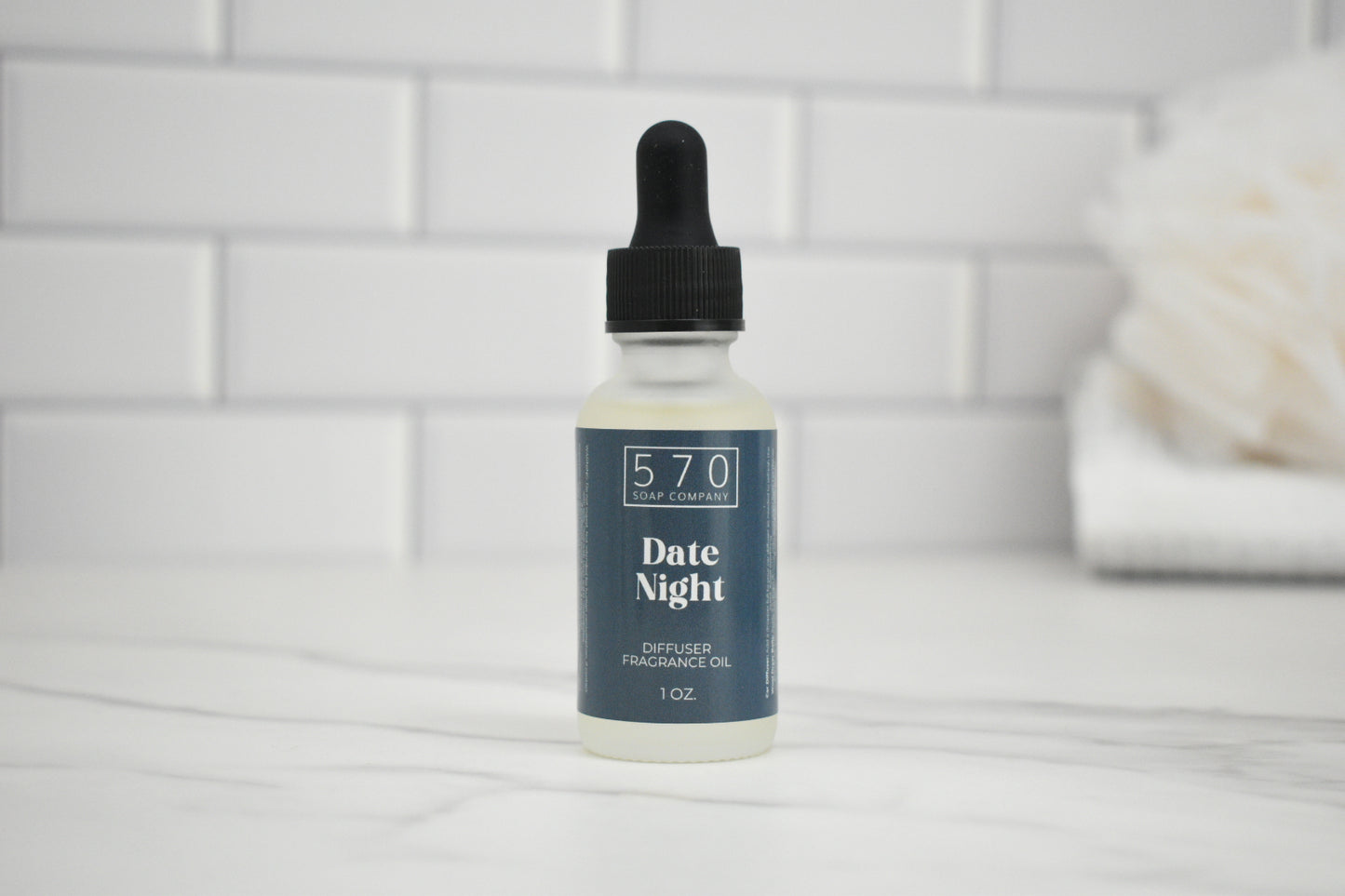 Bottle of 'Date Night' diffuser oil by 570 Soap Company on a white surface with a tiled wall background.