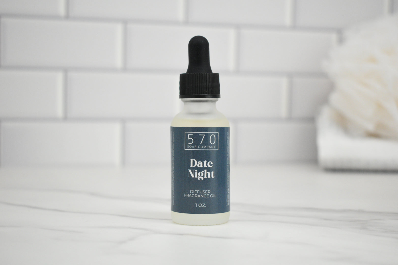 Bottle of 'Date Night' diffuser oil by 570 Soap Company on a white surface with a tiled wall background.