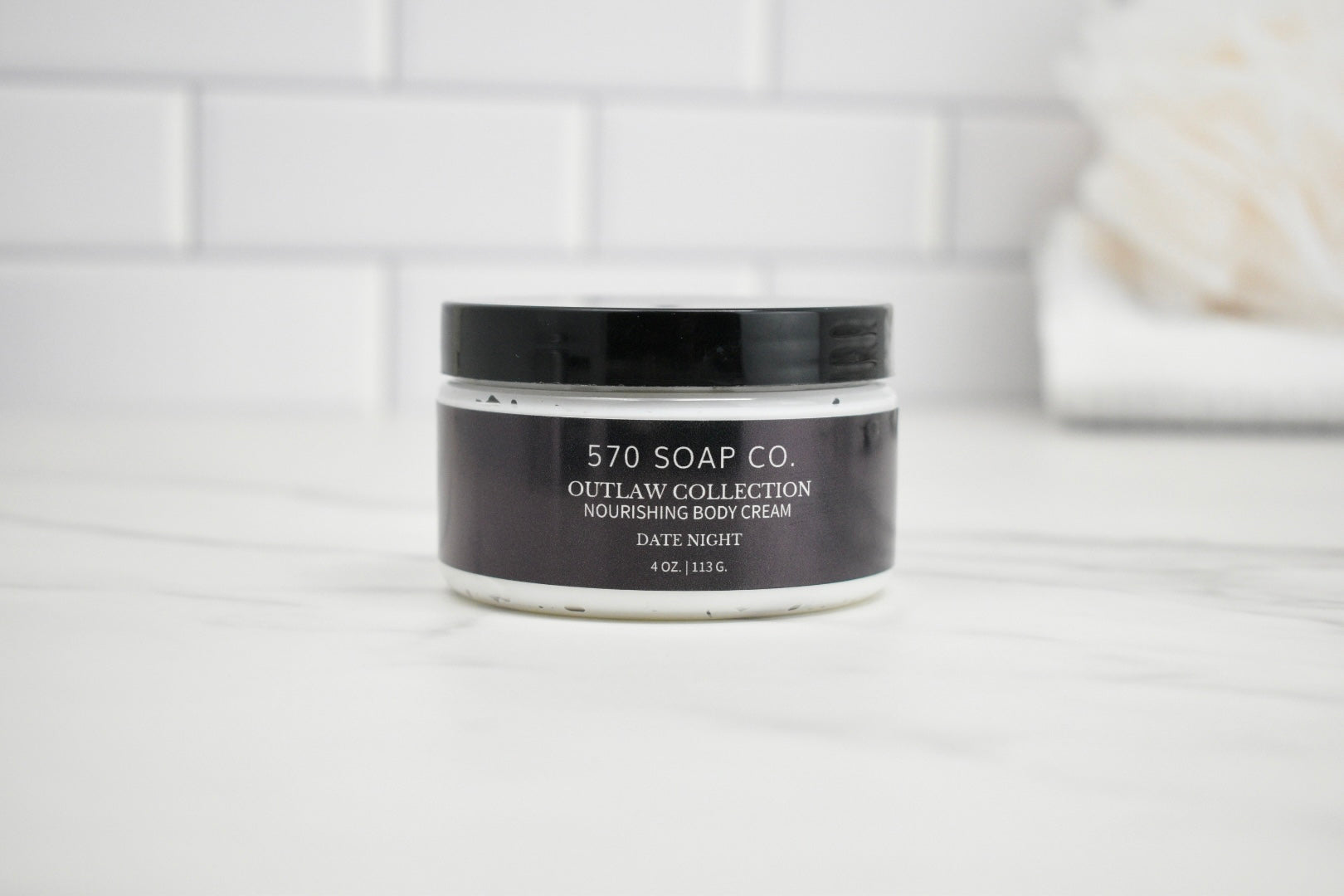 Jar of 570 Soap Co. Outlaw Collection Date Night Nourishing Body Cream on a white surface with a tiled wall background.