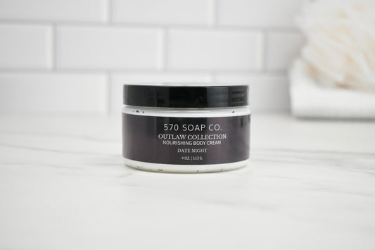 Jar of 570 Soap Co. Outlaw Collection Date Night Nourishing Body Cream on a white surface with a tiled wall background.