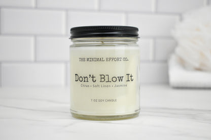Candle jar labeled 'Don't Blow It' by The Minimal Effort Co. on a white surface with a tiled wall background.