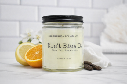 Candle jar with 'Don't Blow It' label on a white surface with lemons and almonds.