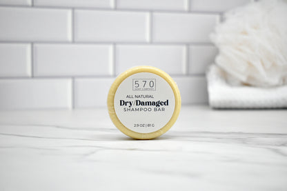 Shampoo bar labeled '570 All Natural Dry Damaged' on a white surface with a tiled wall background.