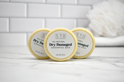 Three all-natural dry damaged shampoo bars on a white tiled surface.