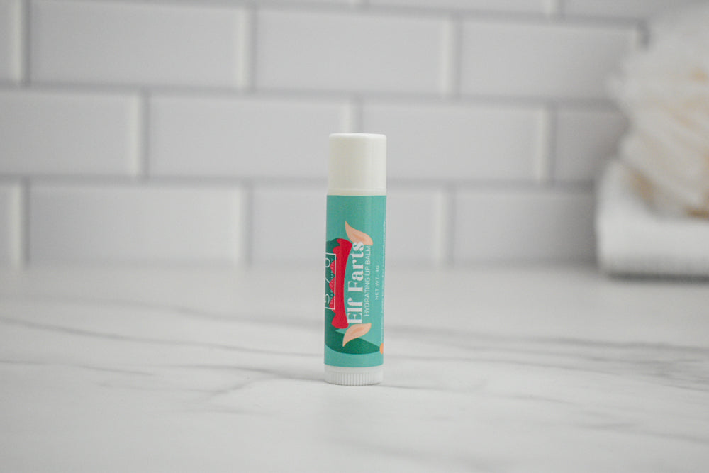 Elf Farts Lip balm stick with a brand logo on a tiled bathroom floor