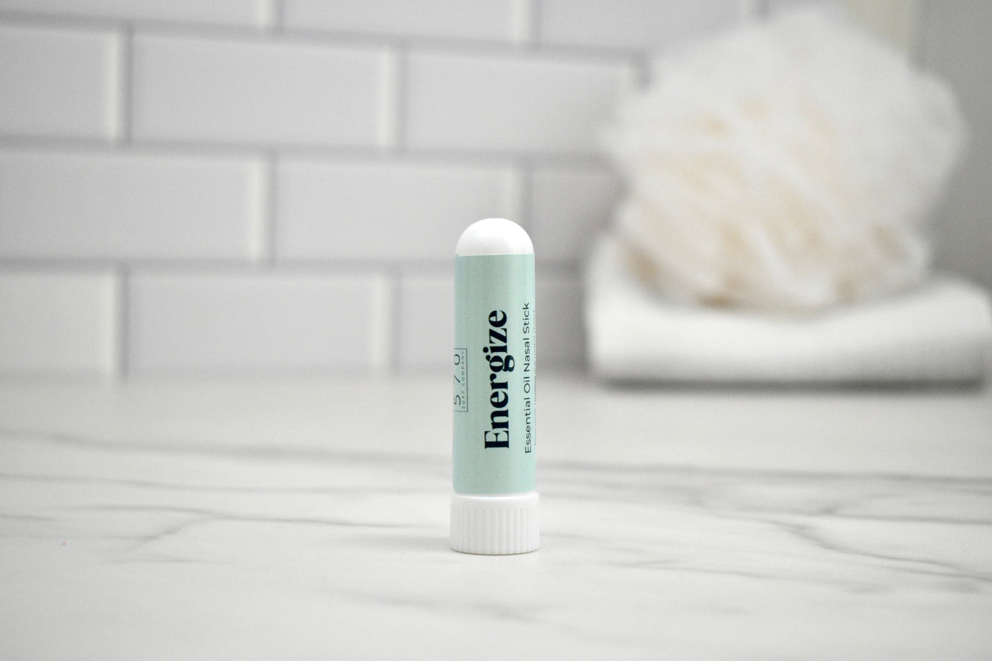 Nasal stick labeled 'Energize' on a bathroom counter with a tiled wall background.