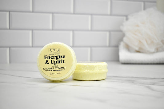 Shower steamer labeled 'Energize & Uplift' on a bathroom counter with a tiled wall background.