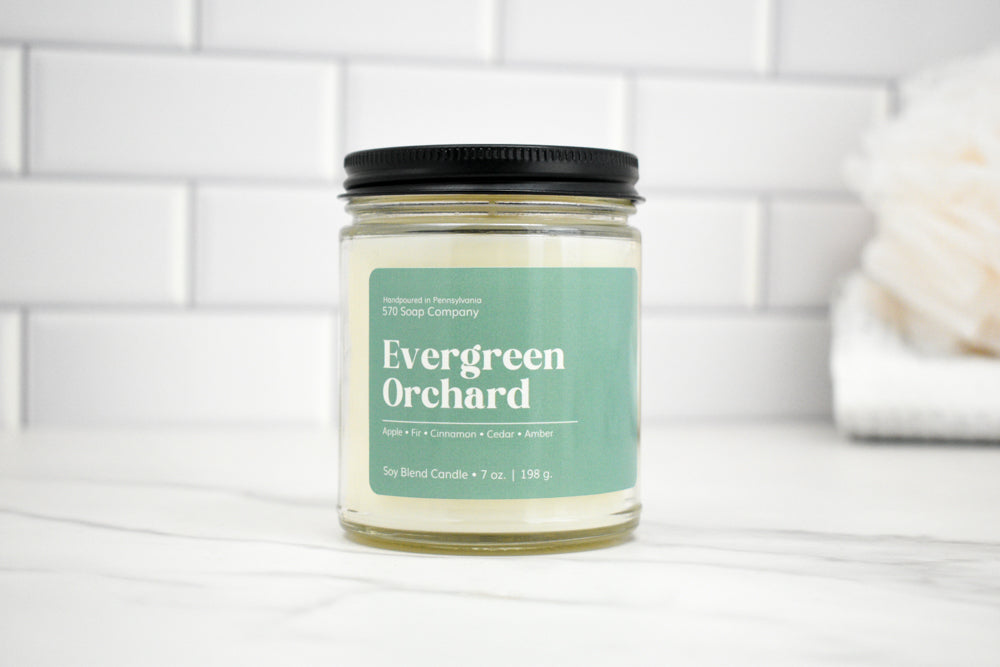 Candle jar labeled 'Evergreen Orchard' on a white surface with a tiled wall background