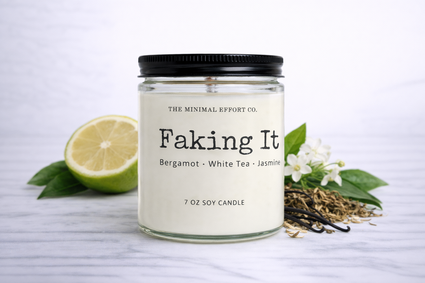 Candle labeled 'Faking It' with a lime, vanilla beans, and flowers on a white background