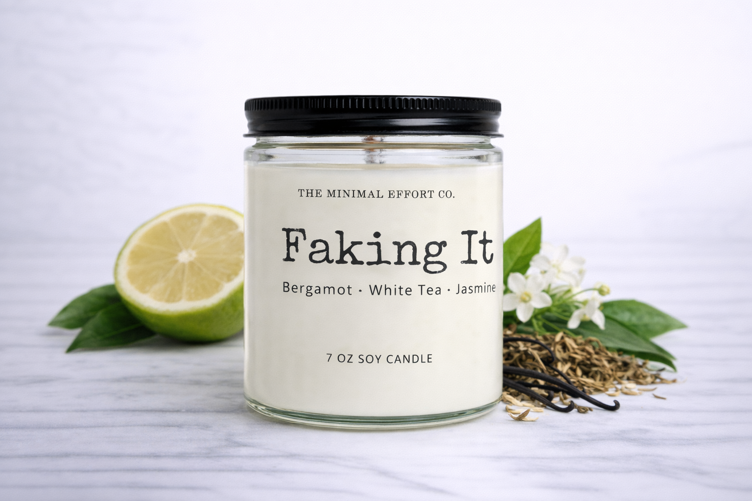 Candle labeled 'Faking It' with a lime, vanilla beans, and flowers on a white background