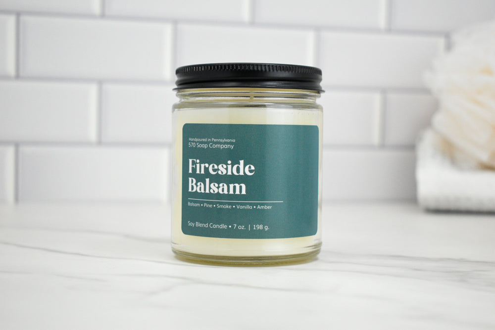Candle jar labeled 'Fireside Balsam' on a white surface with a tiled wall background