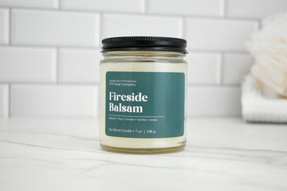 Candle jar labeled 'Fireside Balsam' on a white surface with a tiled wall background