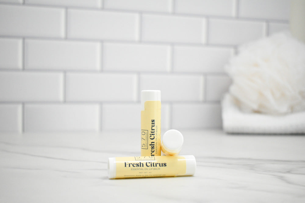 Two lip balms labeled 'Fresh Citrus' on a bathroom counter with a tiled wall background.