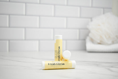 Two lip balms labeled 'Fresh Citrus' on a bathroom counter with a tiled wall background.