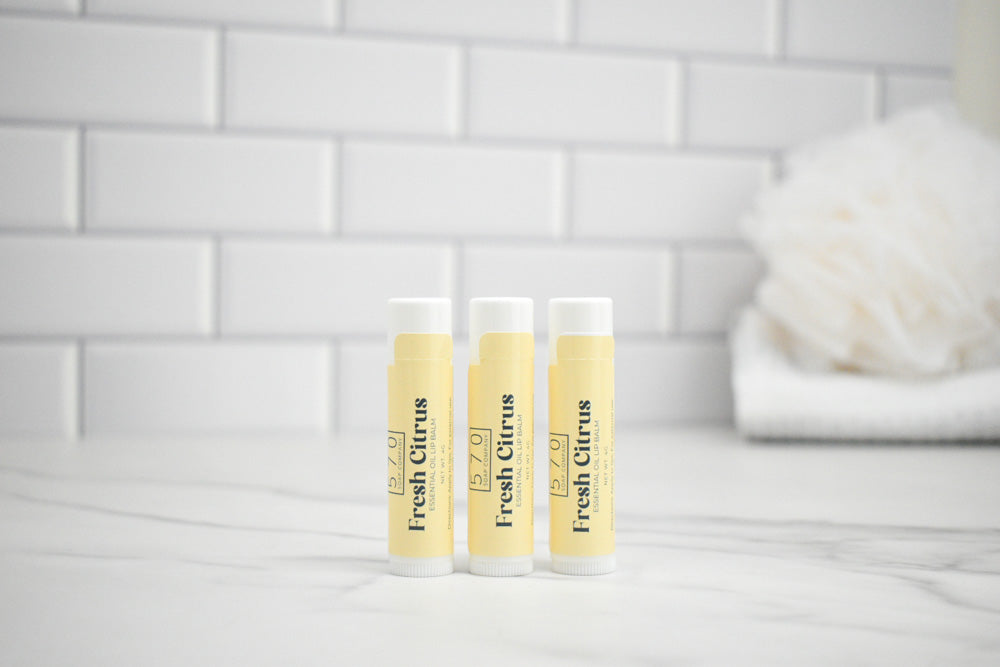 Three lip balm tubes labeled 'Fresh Citrus' on a white surface with a tiled wall background.