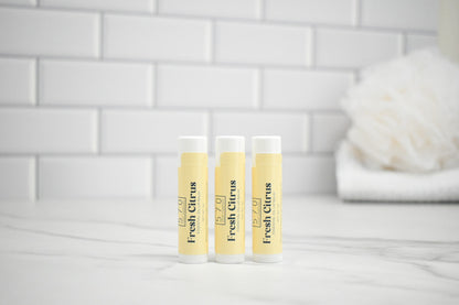 Three lip balm tubes labeled 'Fresh Citrus' on a white surface with a tiled wall background.