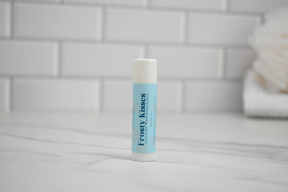 Frosty Kisses lip balm on a tiled bathroom counter.