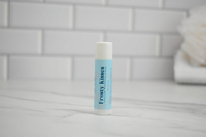 Frosty Kisses lip balm on a tiled bathroom counter.