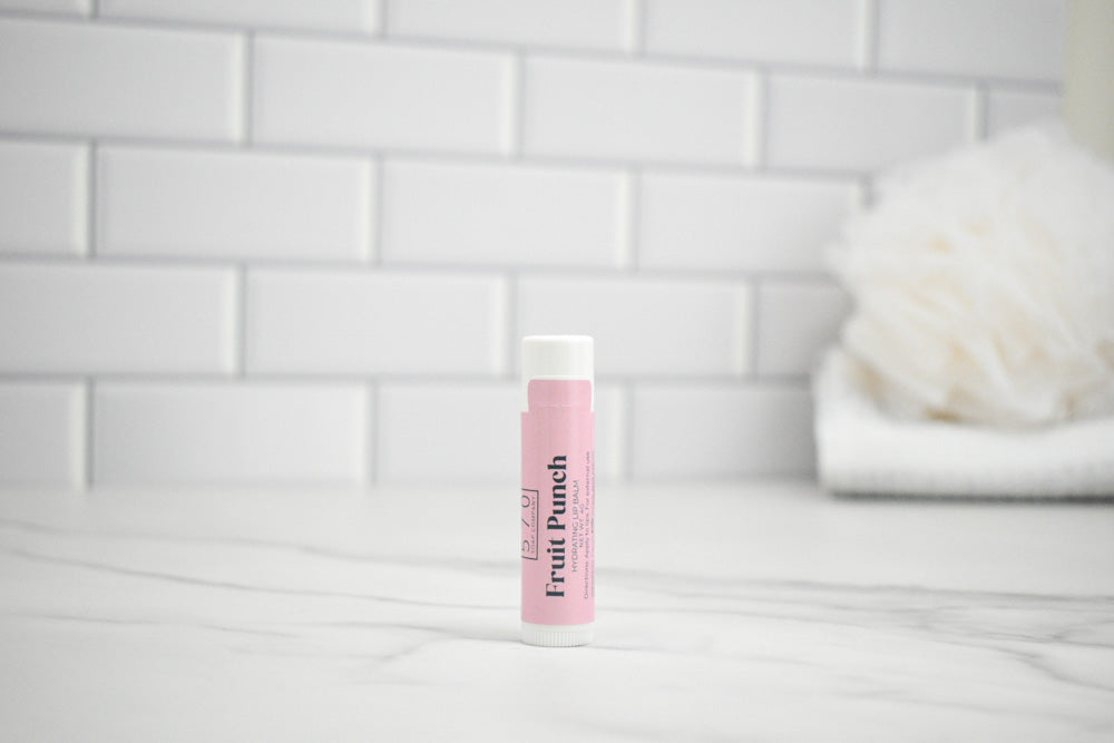 Pink lip balm with 'Fruit Punch' flavor on a white surface with a tiled wall background