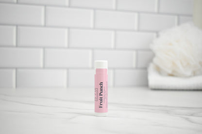 Pink lip balm with 'Fruit Punch' flavor on a white surface with a tiled wall background