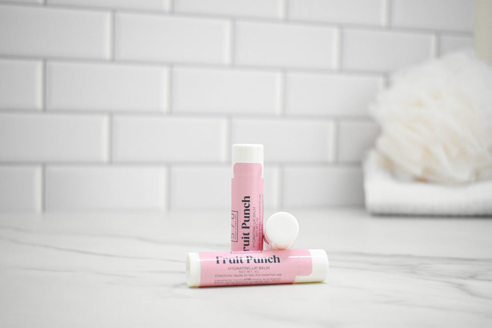 Two pink lip balms labeled 'Fruit Punch' on a white surface with a tiled wall background.