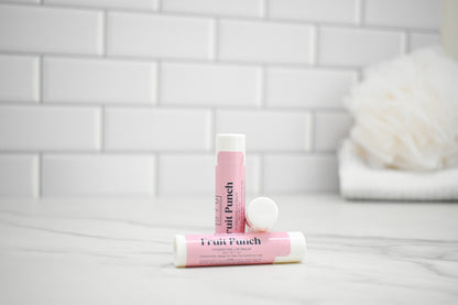 Two pink lip balms labeled 'Fruit Punch' on a white surface with a tiled wall background.
