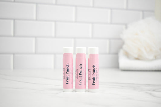 Three lip balm tubes labeled 'Fruit Punch' on a white surface with a tiled wall background.