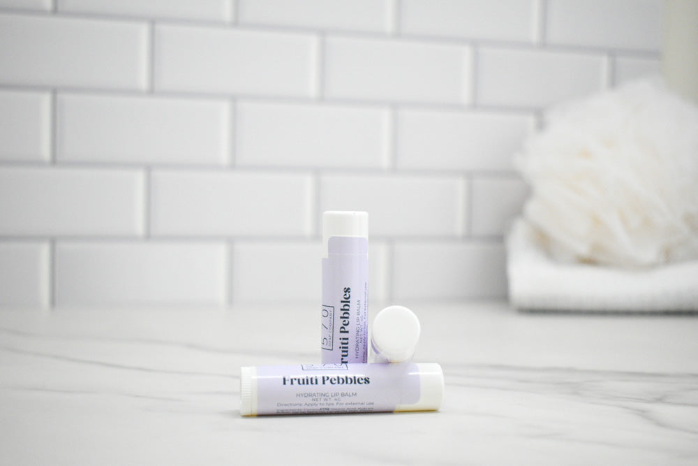 Two lip balm tubes on a bathroom counter with a tiled wall background