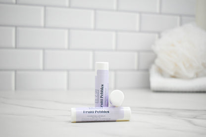 Two lip balm tubes on a bathroom counter with a tiled wall background