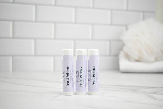 Three lip balms with visible branding on a white surface against a tiled wall background