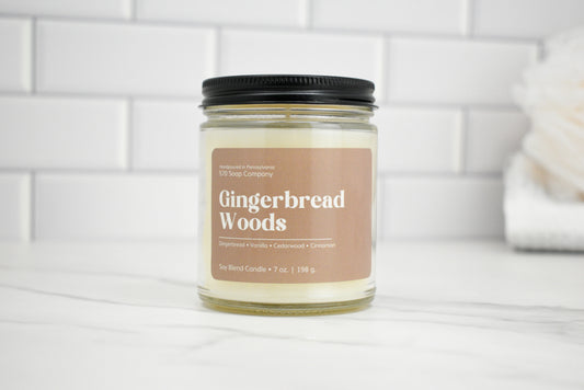 Candle jar labeled 'Gingerbread Woods' on a white surface with a tiled wall background