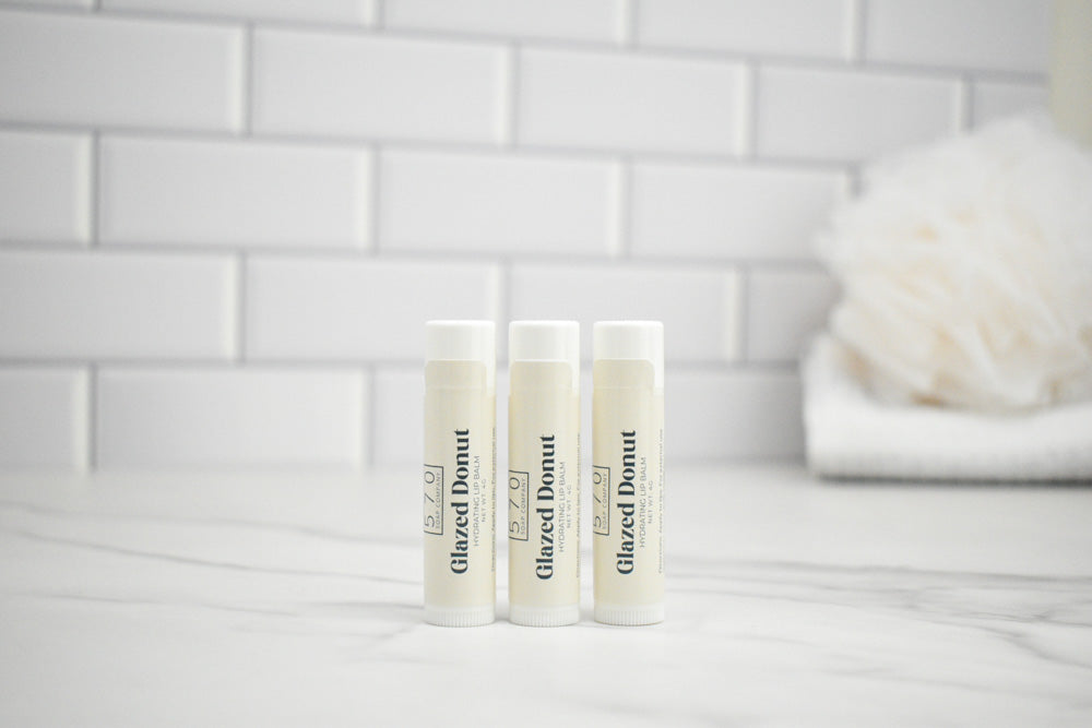 Three lip balm tubes labeled 'Glazed Donut' on a marble surface with a tiled wall background.