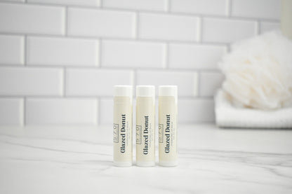 Three lip balm tubes labeled 'Glazed Donut' on a marble surface with a tiled wall background.