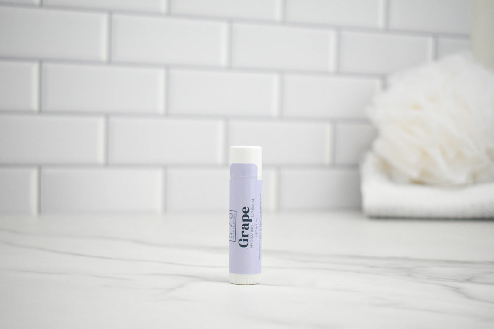 Lip balm with purple packaging on a white surface against a tiled wall background