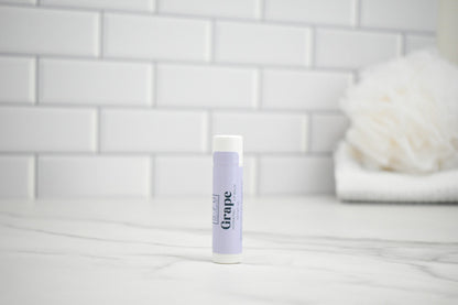 Lip balm with purple packaging on a white surface against a tiled wall background