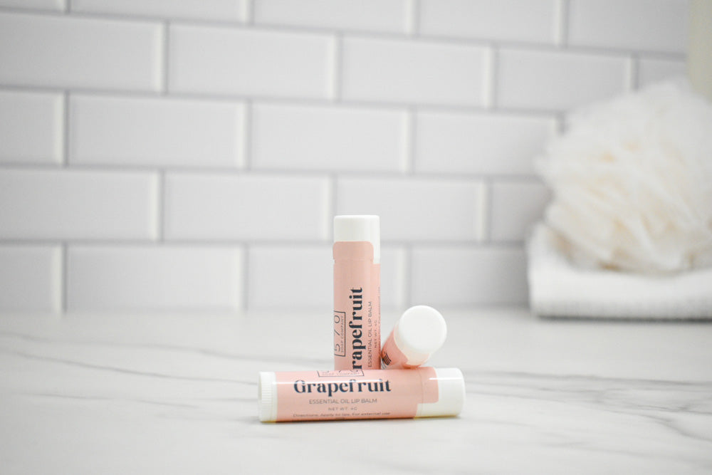 Two lip balms labeled 'Grapefruit' on a light gray surface with a tiled wall background.