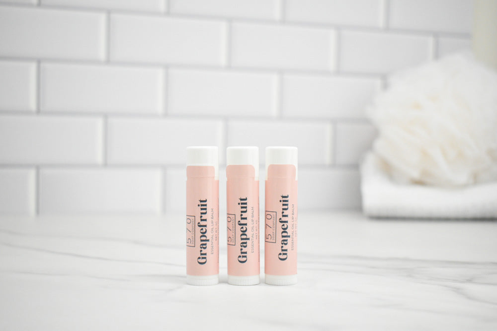 Three lip balm tubes labeled 'Grapefruit' on a bathroom counter with a tiled wall background.